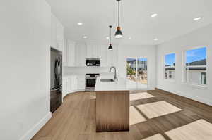 Kitchen with stainless steel appliances, pendant lighting, a kitchen island with sink, white cabinets, and light wood-type flooring