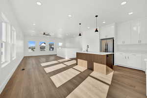 Kitchen featuring stainless steel refrigerator, white cabinetry, pendant lighting, light hardwood / wood-style floors, and a kitchen island with sink