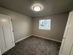 Spare room featuring dark carpet and a textured ceiling