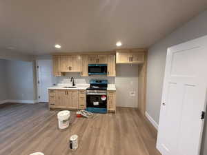 Kitchen with light brown cabinets, light wood-type flooring, sink, and stainless steel range