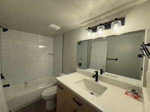 Full bathroom featuring vanity, toilet, a textured ceiling, and tiled shower / bath