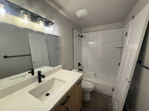 Full bathroom with vanity, hardwood / wood-style flooring, tiled shower / bath combo, toilet, and a textured ceiling