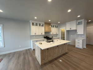 Kitchen featuring light hardwood / wood-style floors, sink, white cabinetry, and a kitchen island with sink