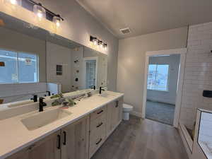 Bathroom with tiled shower, wood-type flooring, vanity, and toilet