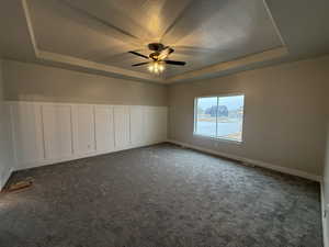 Unfurnished room with ceiling fan, dark carpet, a textured ceiling, and a tray ceiling