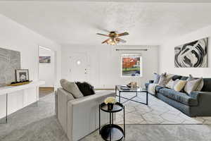 Living room with light carpet, ceiling fan, and a textured ceiling