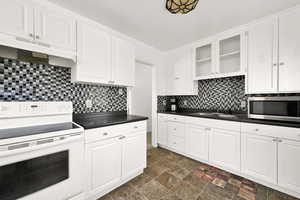 Kitchen with tasteful backsplash, electric range, sink, and white cabinetry