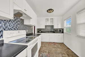 Kitchen with white cabinetry, decorative backsplash, electric range, and sink