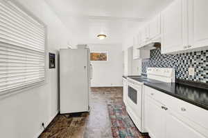 Kitchen featuring white cabinets, decorative backsplash, and white appliances