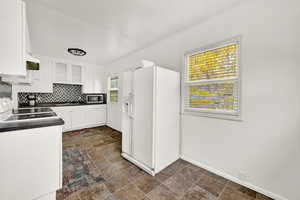 Kitchen featuring white refrigerator with ice dispenser, white cabinetry, a wealth of natural light, and black range oven