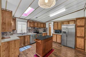 Kitchen featuring sink, a center island, dark hardwood / wood-style flooring, vaulted ceiling with skylight, and appliances with stainless steel finishes