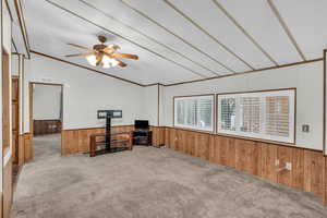 Carpeted office featuring ceiling fan, wood walls, ornamental molding, and lofted ceiling