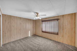 Carpeted spare room with ceiling fan and wooden walls