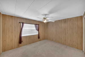 Carpeted spare room featuring ceiling fan and wooden walls