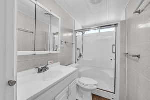 Bathroom with a textured ceiling, a shower with door, vanity, and tile walls