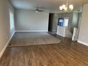 Spare room featuring ceiling fan with notable chandelier and dark wood-type flooring