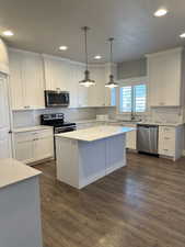 Kitchen with stainless steel appliances, dark wood-type flooring, pendant lighting, white cabinetry, and a kitchen island