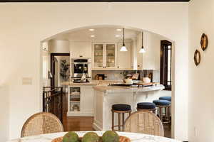 Kitchen with backsplash, stainless steel oven, decorative light fixtures, dark hardwood / wood-style floors, and white cabinetry