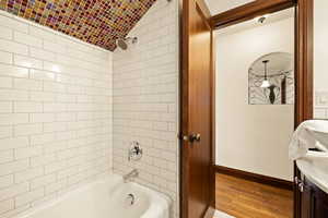 Bathroom featuring vanity, tiled shower / bath, vaulted ceiling, and hardwood / wood-style flooring