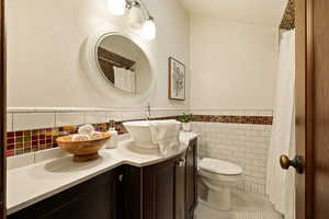 Bathroom featuring tile patterned flooring, vanity, toilet, and tile walls