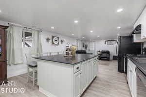 Kitchen with light hardwood / wood-style flooring, stainless steel dishwasher, ventilation hood, a breakfast bar, and white cabinets