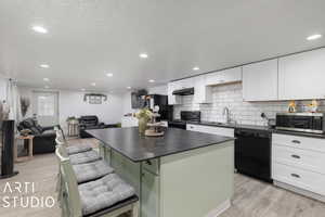 Kitchen with a center island, a kitchen breakfast bar, light hardwood / wood-style flooring, white cabinets, and black appliances