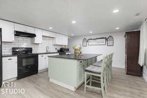 Kitchen featuring black electric range, light wood-type flooring, white cabinetry, and a kitchen island