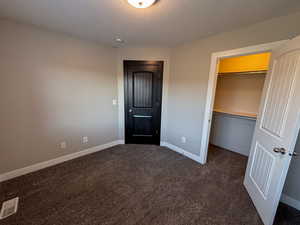 Bedroom with dark colored carpet, a textured ceiling, a walk-in closet, and a closet