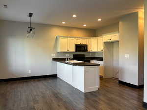 Kitchen with black appliances, kitchen peninsula, white cabinetry, and hanging light fixtures