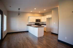 Kitchen featuring black range with electric cooktop, dark LVP / wood-style flooring, kitchen peninsula, decorative light fixtures, and white cabinets