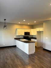 Kitchen with black appliances, dark LVP / wood-style floors, white cabinetry, and hanging light fixtures