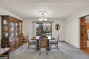 Carpeted dining area with a notable chandelier and sliding doors to deck.