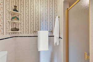 Main suite bathroom featuring tile walls, an enclosed shower, and toilet