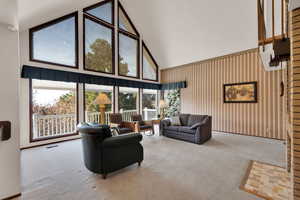 Living room with carpet flooring, high vaulted ceiling and large windows with views.