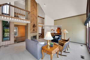 Carpeted living room with high vaulted ceiling and a brick fireplace and open loft.