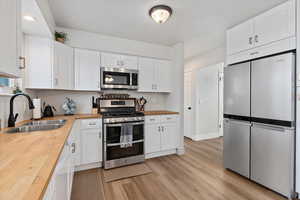 Kitchen with wooden counters, appliances with stainless steel finishes, and white cabinets