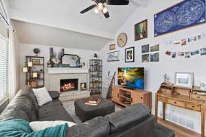 Living room featuring ceiling fan, a fireplace, lofted ceiling with beams, and wood-type flooring