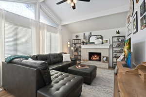 Living room featuring vaulted ceiling with beams, ceiling fan, light hardwood / wood-style floors, and a brick fireplace