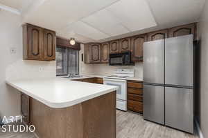 Kitchen with white electric range, kitchen peninsula, light hardwood / wood-style floors, dark brown cabinetry, and stainless steel refrigerator