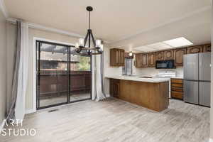 Kitchen featuring white electric range, a notable chandelier, light hardwood / wood-style floors, kitchen peninsula, and stainless steel refrigerator