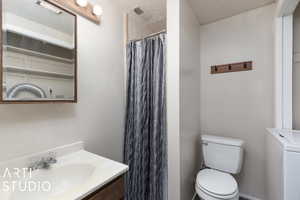 Bathroom with a shower with curtain, a textured ceiling, vanity, washer / dryer, and toilet