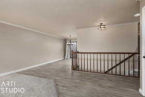 Unfurnished room featuring a textured ceiling, hardwood / wood-style flooring, crown molding, and a notable chandelier