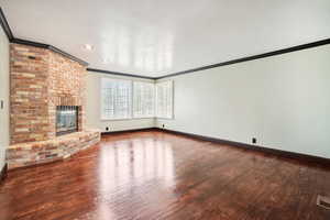 Unfurnished living room with hardwood / wood-style floors, a textured ceiling, a brick fireplace with gas log, plantation shutters and crown molding