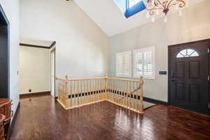 Entrance foyer featuring a notable chandelier, a skylight, wood-type flooring, and high vaulted ceiling