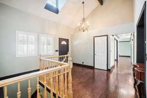 Foyer featuring dark hardwood / wood-style flooring, a skylight, high vaulted ceiling, a notable chandelier, and beamed ceiling