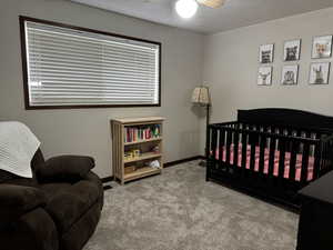 Carpeted bedroom featuring a textured ceiling, ceiling fan, and a crib