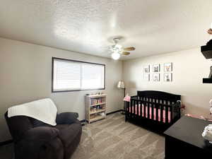 Carpeted bedroom with ceiling fan, a crib, and a textured ceiling