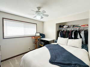 Carpeted bedroom featuring ceiling fan, a textured ceiling, and a closet