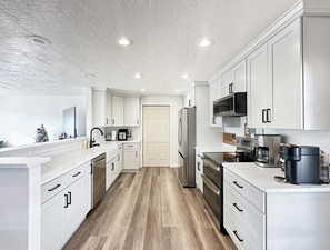 Kitchen featuring kitchen peninsula, appliances with stainless steel finishes, a textured ceiling, and white cabinetry