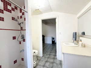 Bathroom featuring a tile shower, a textured ceiling, toilet, and lofted ceiling